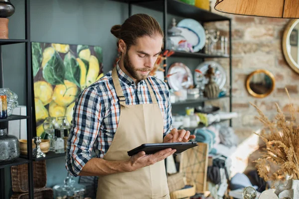 Hombre enfocado que trabaja en la tableta mientras está de pie en la tienda de decoración —  Fotos de Stock