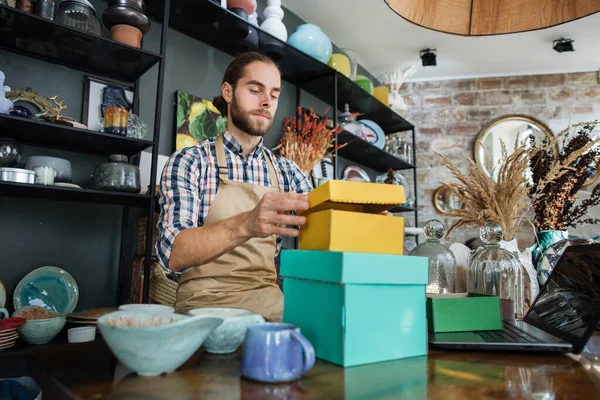 Boîtes d'emballage de vendeur barbu avec des marchandises au magasin de décoration — Photo