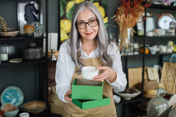 Aged woman packing white candle in green box at store — Stock Photo, Image