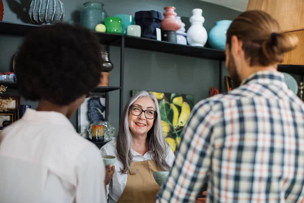 Aged saleswoman consulting multiracial couple at decor store — Stock Photo, Image