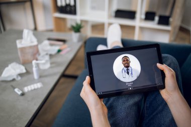 Kanepede oturan ve evdeki Afrikalı Amerikalı erkek doktorla video görüşmesi yapan kadın hastaların el taramaları.