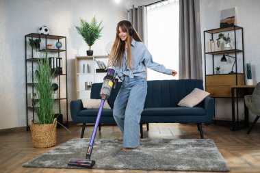 Kadın müzik dinliyor ve elektrik süpürgesiyle ev işleri yapıyor.