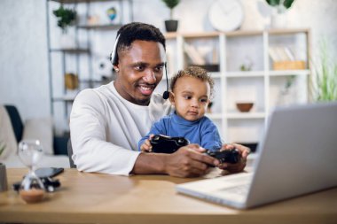 Afro-Amerikan baba ve oğlu laptopta oyun oynuyorlar.