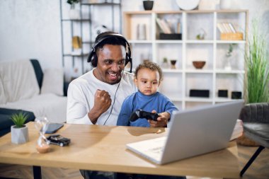 Afrikalı adam ve çocuk bilgisayar ve joystick kullanarak oyun oynuyorlar.