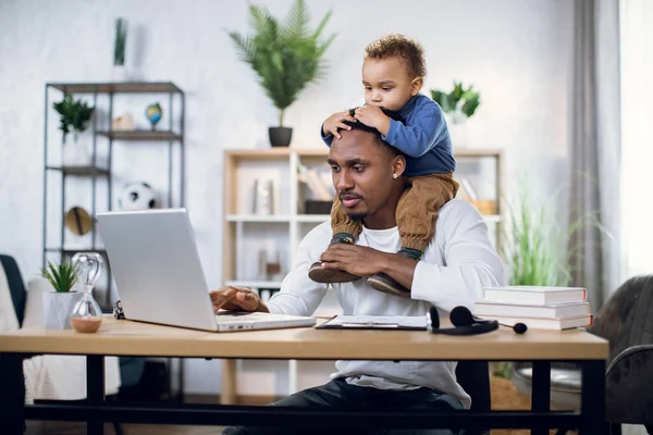 Afro americano hombre con hijo en el cuello trabajando en portátil — Foto de Stock