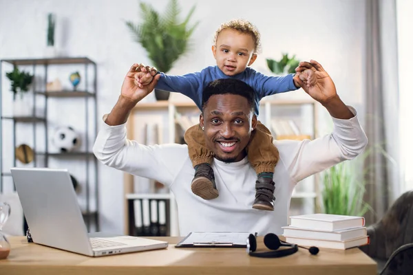 Afro-americano pai com filho no pescoço trabalhando em casa — Fotografia de Stock