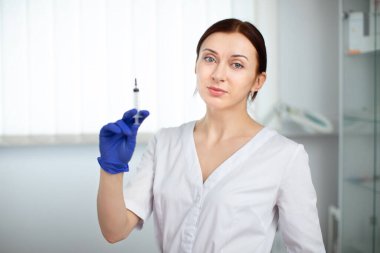 Kendine güvenen profesyonel kadın kozmetolojistin portresi modern tıbbi estetik ofis salonunda duruyor, elinde güzellik enjeksiyonlu bir şırınga tutuyor..