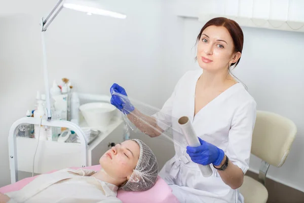 Tratamiento del problema de la piel del acné en la clínica de cosmetología. Mujer esteticista médico sostiene la película de plástico, listo para ponerlo en la cara de la niña antes del procedimiento de terapia del acné. —  Fotos de Stock