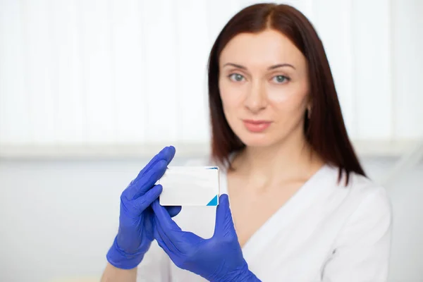 의학, 우주론, 미 그리고 사람들의 개념. 흰색 제복을 입고 푸른색 장갑을 끼고 의약품 상자를 들고 있는 젊은 전문 여성 미용사 피부과 의사의 사진을 클로즈업. — 스톡 사진
