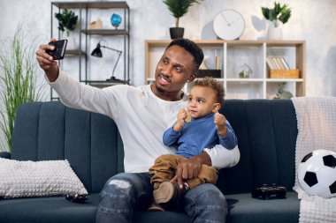 Mutlu baba ve oğul evde akıllı telefondan selfie çekiyorlar.