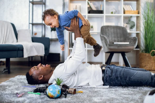 Hombre alegre acostado en la alfombra y jugando con el niño — Foto de Stock