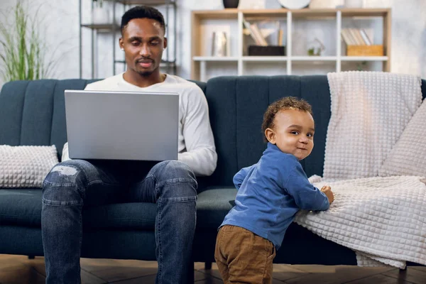 Hombre afroamericano trabajando en laptop y cuidando de su hijo — Foto de Stock