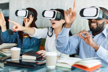 Eski ve yeni teknolojiler, geleneksel ve dijital. Heyecanlı, yaratıcı, etnik çeşitlilikte üç arkadaş, VR kulaklıklarıyla oturmuş, gülüyor ve modern kafede vakit geçiriyorlar..