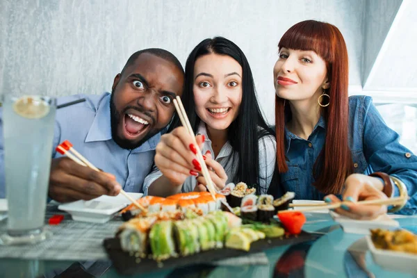 사람, 음식, 그리고 우정의 개념. 일본의한 식당에서 초밥을 즐기는 행복 한 세 명의 젊은 친구. 행복 한 학생들은 초밥 롤을 먹고 카메라 앞에서 웃는다. — 스톡 사진