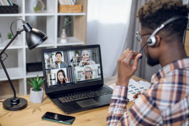 Çeşitli ortaklarla video görüşmesi için dizüstü bilgisayar kullanan siyahi bir adam