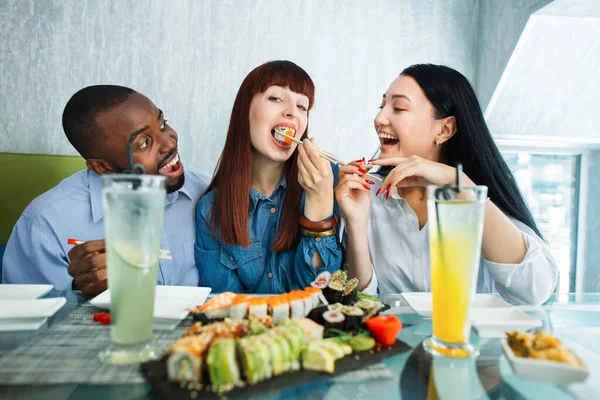 초밥의 컨셉, 해산물, 아시아인의 음식. 카프카스 계와 아시아 계젊은 친구 세 명 이 식당에 앉아 맛있는 초밥을 먹으면서. — 스톡 사진