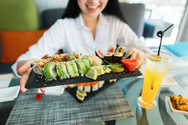 Koncept jídla, tradiční japonské jídlo. Žena si užívá čerstvého sushi v luxusní restauraci. Klientka drží talíř s orientálním sushi jídlem na obědě. Soustřeď se na role. — Stock fotografie