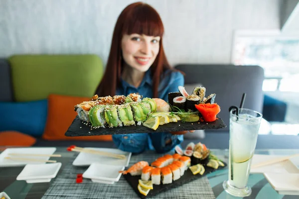 Koncept jídla, tradiční japonské jídlo. Příjemná dívka těší chutné sushi v luxusní restauraci. Klientka drží talíř s orientálním sushi jídlem na obědě. Soustřeď se na role. — Stock fotografie