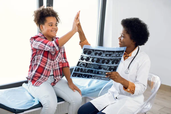 건강 과 아이들. 방사선 , MRI, 계산 된 단층 촬영 , X-ray 컨셉. 친절 한 아프리카 의사가 12 세의 젊은 여성 혼혈아에게 X-ray CT 사진을 보여 주고 있고, 5 명에게 도고 혈압을 주고 있습니다.. — 스톡 사진