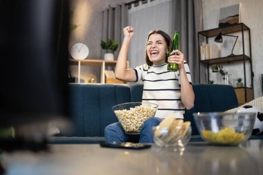 Biralı ve abur cuburlu bir kadın TV 'de maç izliyor.