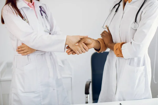 保健、协议和雇用概念。在现代医院里，两位难以辨认的专业、多种族、多样化的女医生手拉手，手拉手. — 图库照片