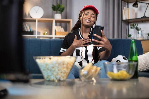 Mulher africana assistindo futebol na TV e usando smartphone — Fotografia de Stock