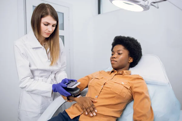 Cancro della pelle e prevenzione del melanoma. Medico dermatologo professionista esamina i pazienti talpe sul braccio della signora africana con l'aiuto di un dispositivo moderno per la dematoscopia. — Foto Stock