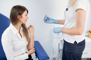 Modern tıp laboratuarındaki laboratuvar teknisyeni ve kadın hasta. Tanınmayan kadın hemşire, test tüpünü hastaya kan örneğiyle gösteriyor. Koltuğunda oturan Avrupalı genç bir kadın..