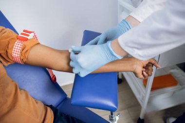 Modern klinikte hastayı kan alımına hazırlayan kadın doktorun eli yakın çekim. Sandalyede oturan Afrikalı hasta kan testine hazır..