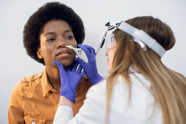 У сучасній клініці видно жіноче плече лікаря молодої хворої жінки-африканки під час перевірки носа. Лікування синуситом, діагностика та лікування носових захворювань.. — стокове фото