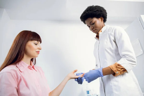 Jovem médica afro-americana concentrada fazendo análises de coleta de sangue para sua paciente caucasiana no hospital moderno. Análise sanguínea, teste de grupo, VIH, hepatite. — Fotografia de Stock