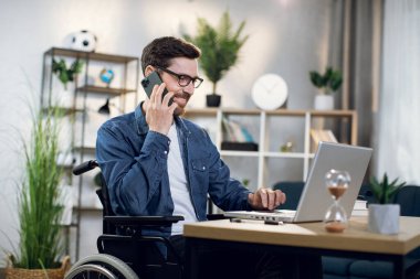 Cep telefonuyla konuşan ve bilgisayarla çalışan engelli adam.