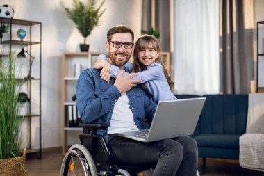Tekerlekli sandalyede oturan kızı babasına sarılıyor.