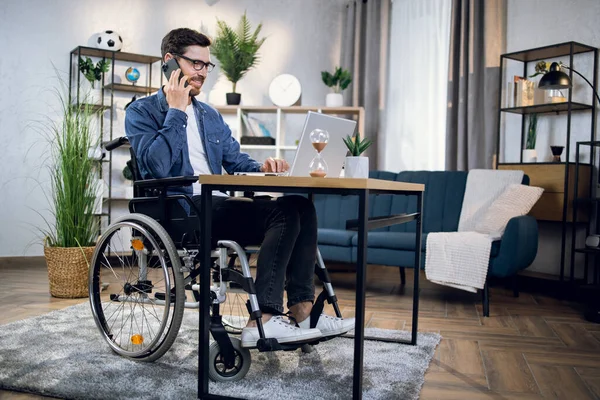 Homem com deficiência conversando no celular e trabalhando no laptop — Fotografia de Stock