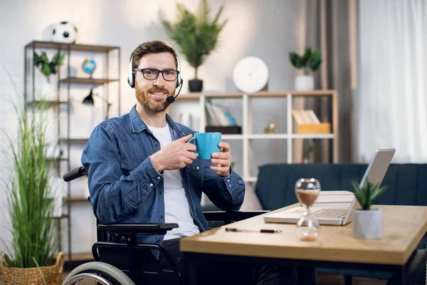 Handicapped man drinking coffee while working on laptop
