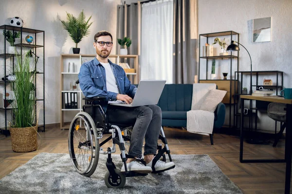 Young male freelancer sitting in wheelchair and using laptop
