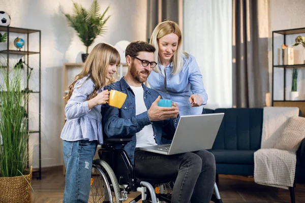 Mujer y niño cerca del hombre en silla de ruedas con portátil — Foto de Stock