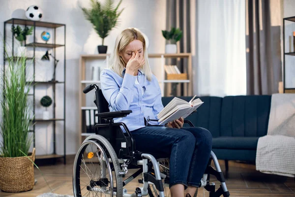 Woman in wheelchair rubbing eyes after long read of book