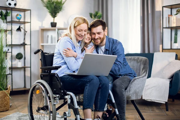 Man en kind knuffelen vrouw in rolstoel met laptop — Stockfoto