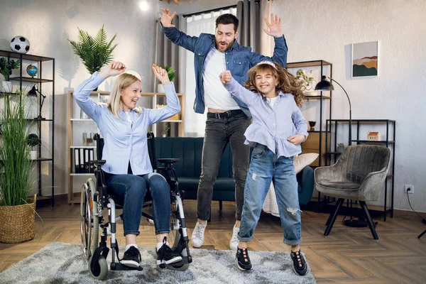 Woman in wheelchair dancing with husband and daughter