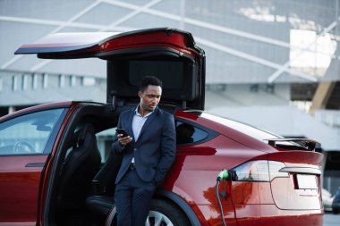 İşadamı elektrikli arabayı şarj ederken cep telefonuyla çalışıyor