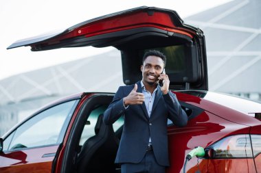 Şarj olan arabanın yanında duran ve cep telefonuyla konuşan adam.