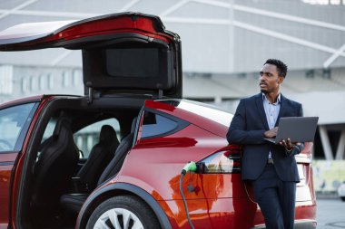 Afrikalı işadamı dizüstü bilgisayarda çalışıyor ve araba şarj ediyor