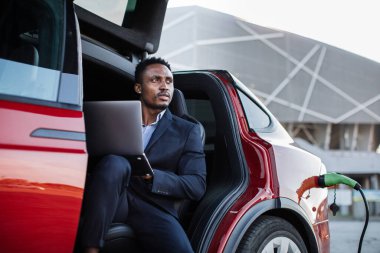 Bilgisayarlı bir adam içeride oturmuş elektrikli arabayı şarj ediyor.