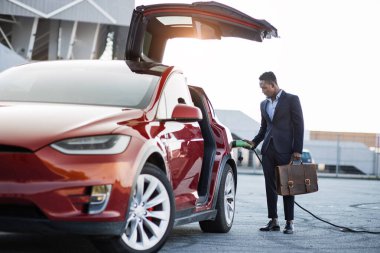 Bavullu Afrikalı işadamı elektrikli arabayı şarj ediyor