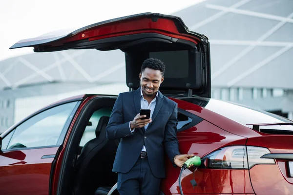 Hombre de traje usando el teléfono celular mientras espera a que el coche se cargue —  Fotos de Stock