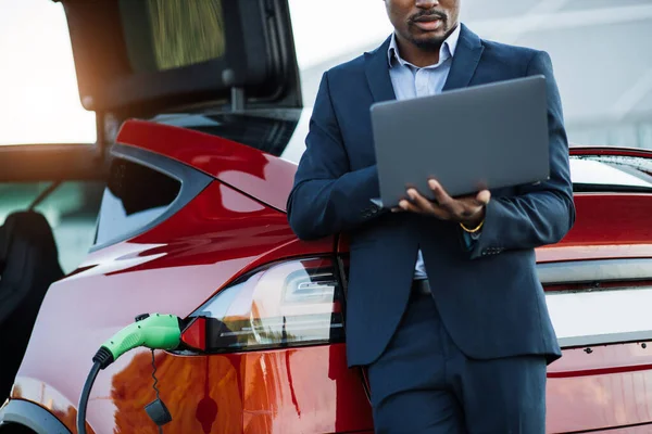 Homme africain utilisant un ordinateur portable tout en rechargeant la batterie de la voiture — Photo