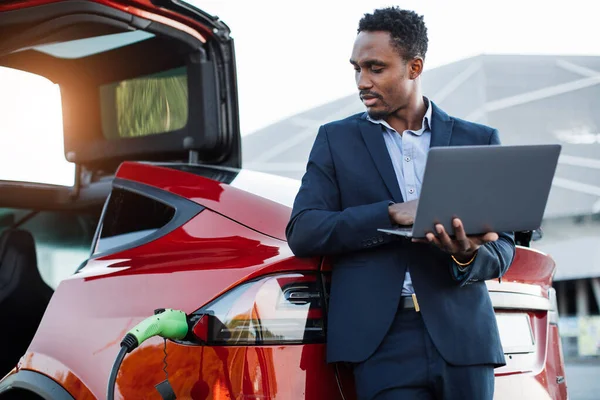 Afrikansk affärsman som arbetar på bärbar dator och laddar bilen — Stockfoto