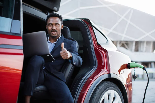 Geschäftsmann lädt Auto und arbeitet am Laptop — Stockfoto