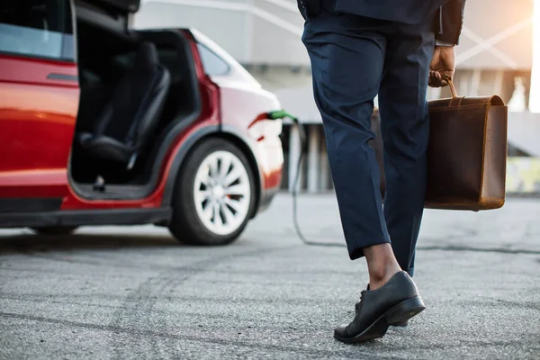 Homme avec valise debout près de la voiture électrique qui charge — Photo